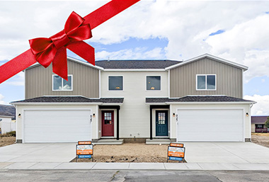 Attractive white, tan and grey twin homes with contrasting red and green-blue front doors - new builds by Smart Dwellings in Rawlins, WY. A red bow is across the top left corner of the photo.